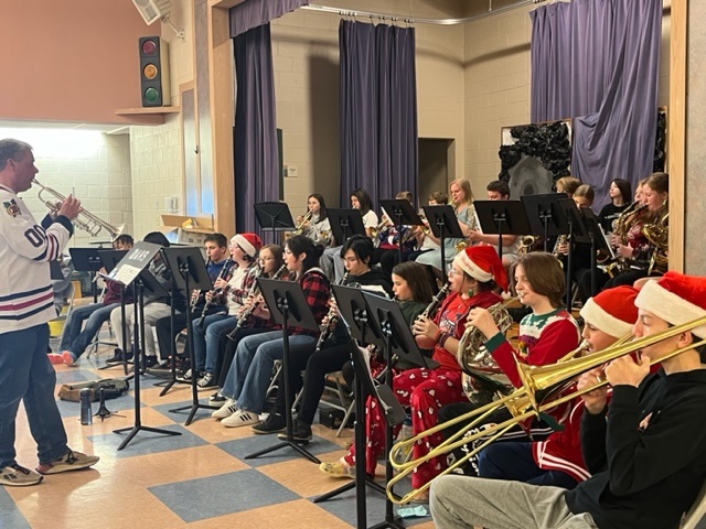 A band performing in a school hall with the conductor.