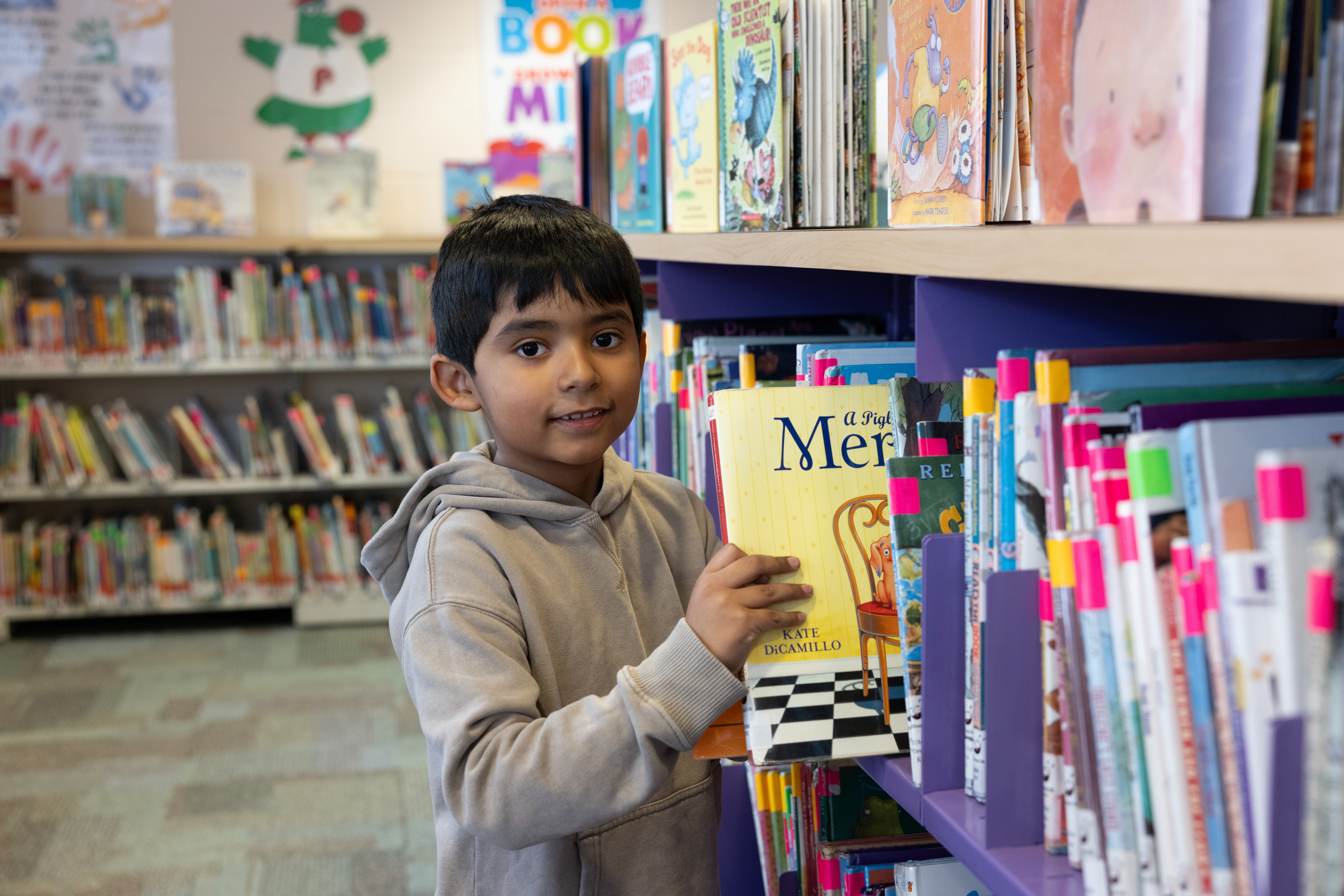 little boy in library pulling book off of shelf