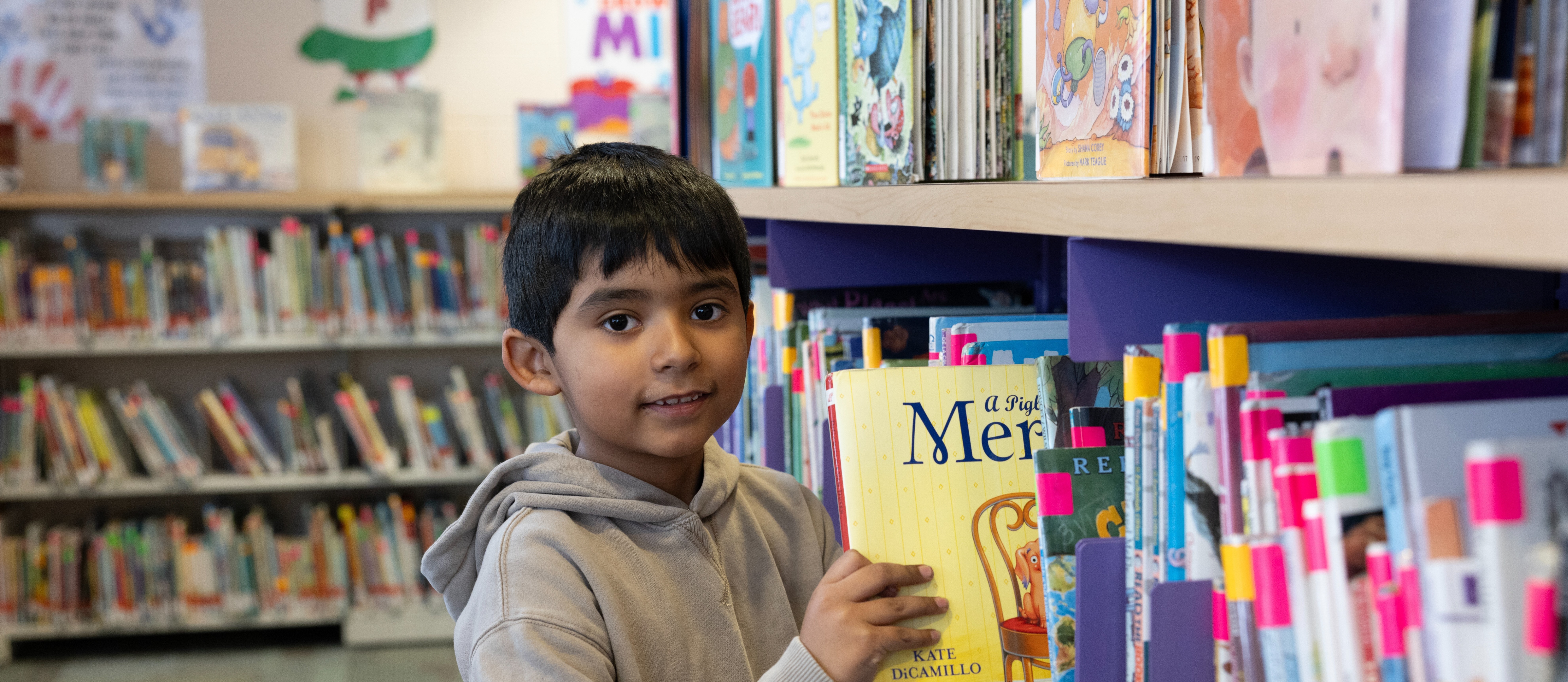 little boy in library pulling book off of shelf