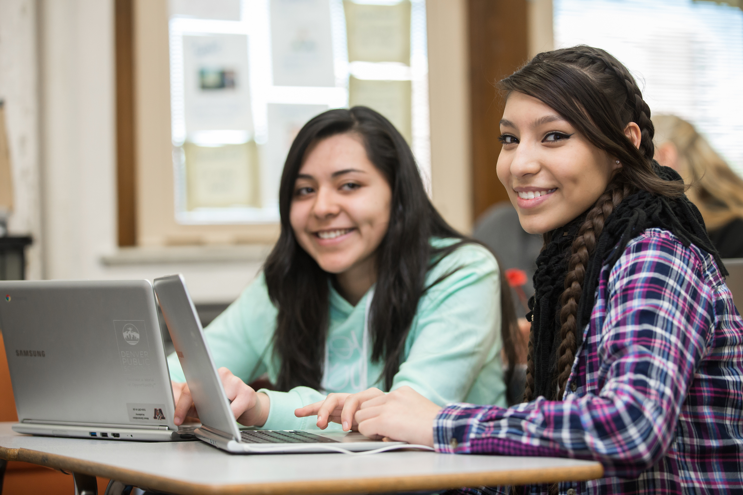 Two teen girls smiling while using laptop