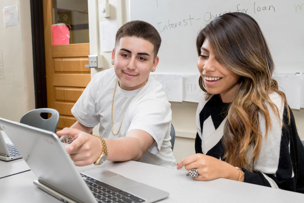 High school student and teacher smiling while looking at laptop