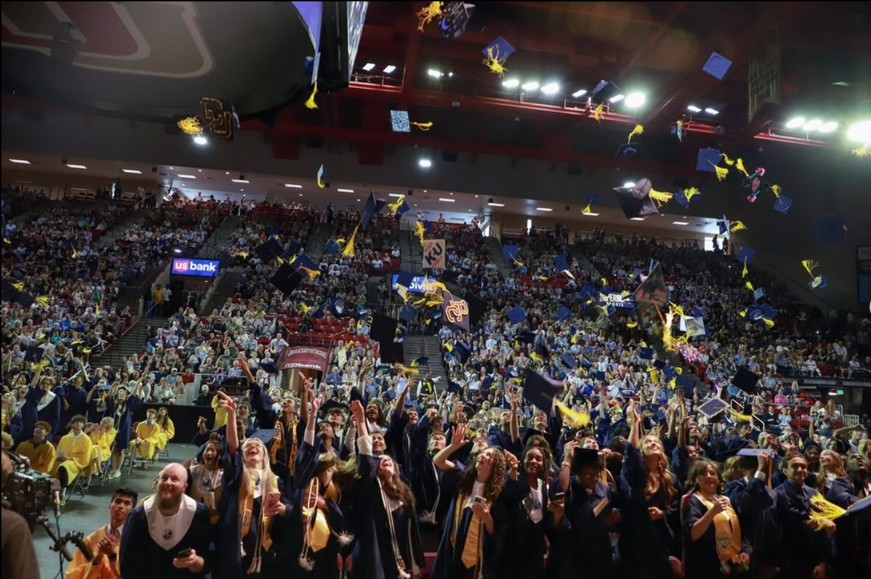 Students in graduation gowns toss caps in the air