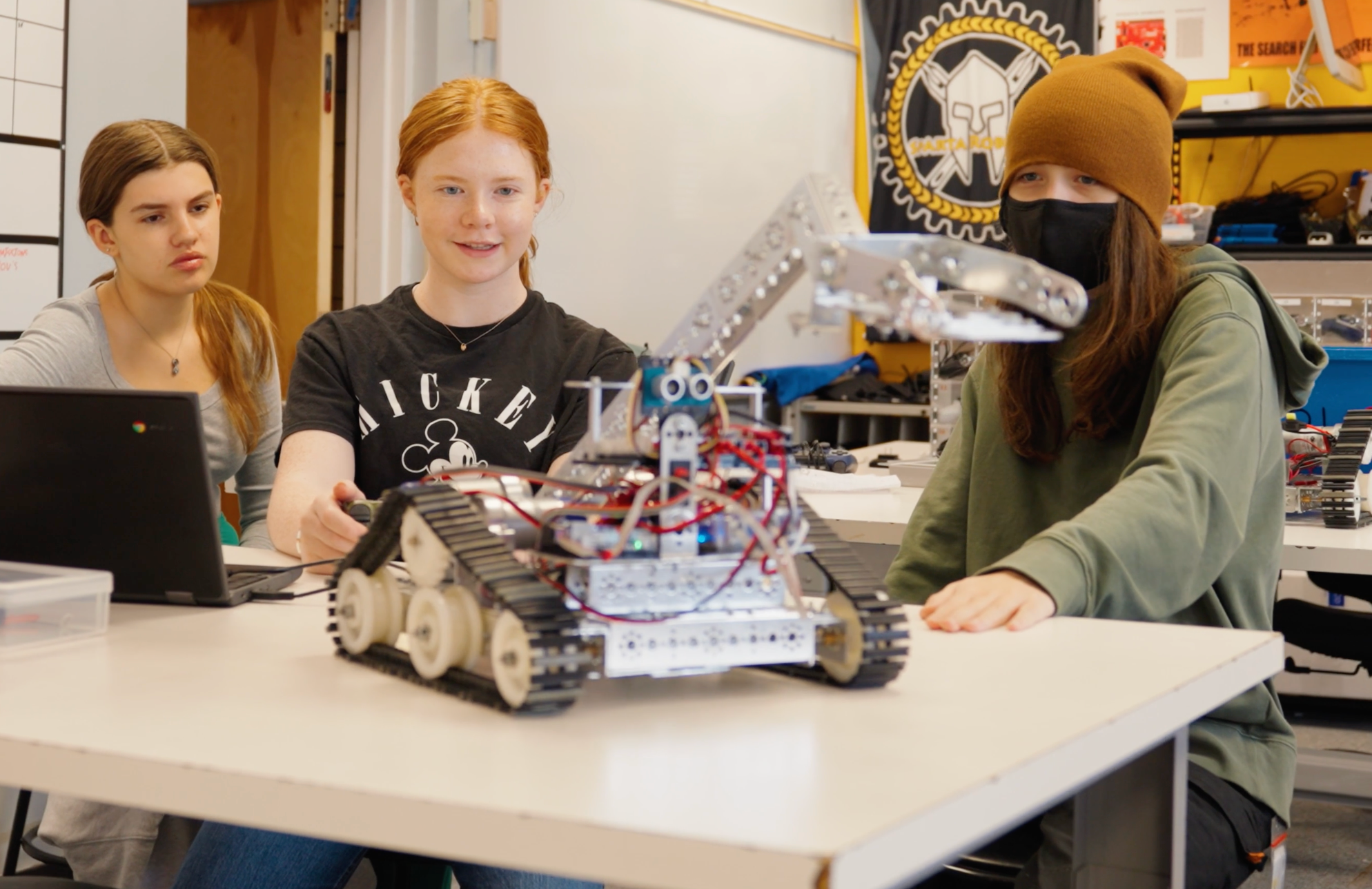 three students work on their fully functional robot  at their desk.