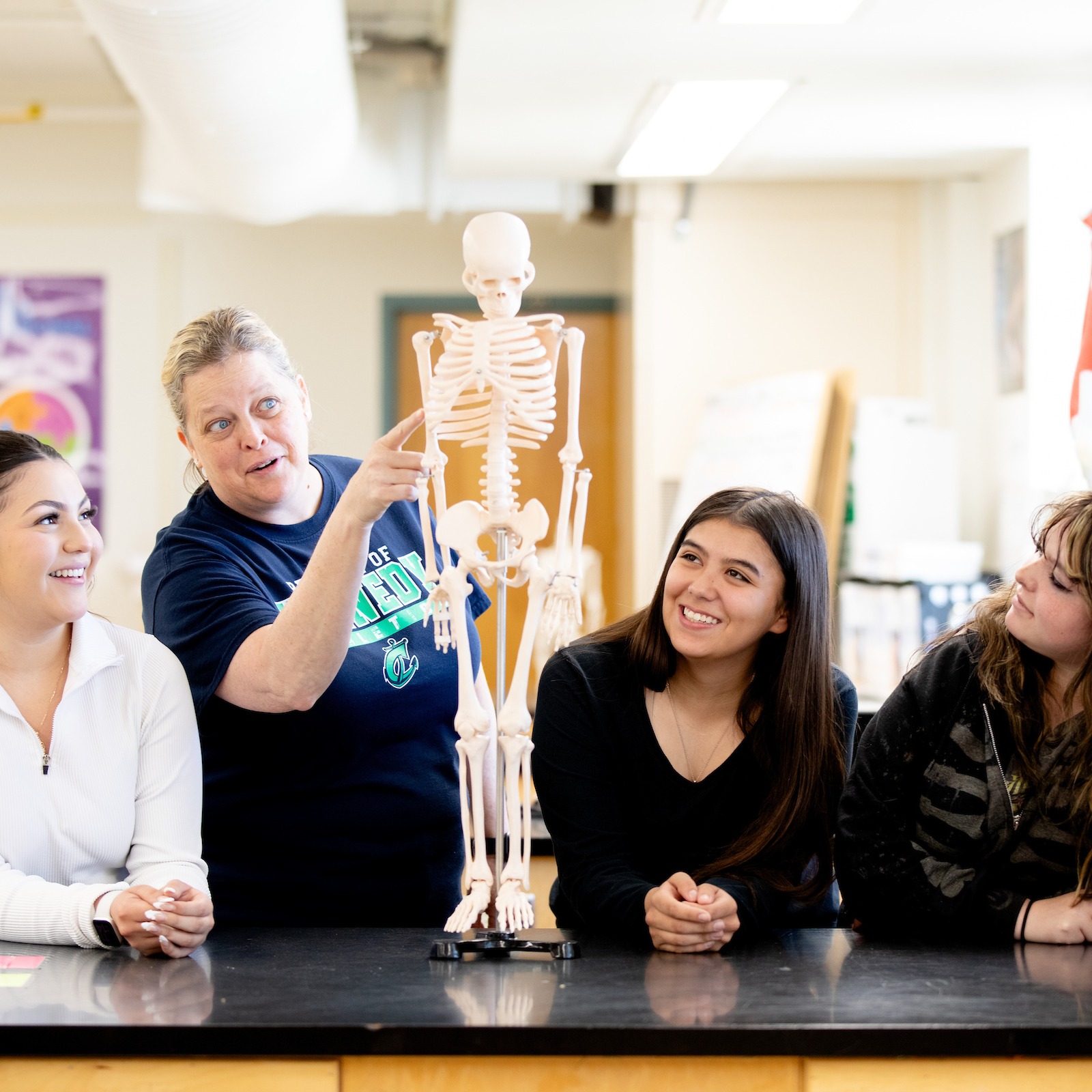 Teacher instructing three students with skeletal model