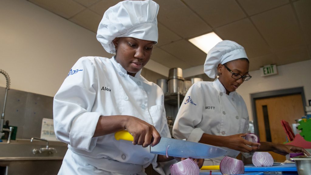 Two teen girls slicing onions wearing a chef uniform