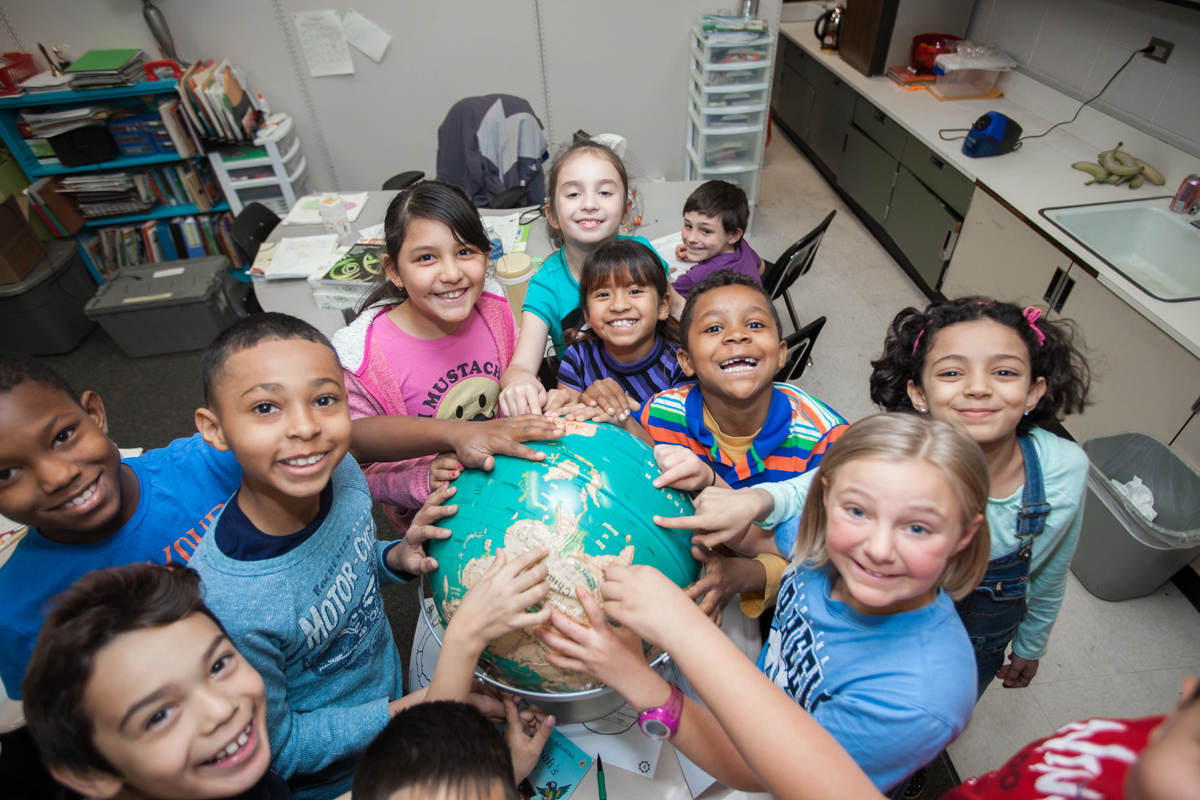 kids smiling to camera and pointing at a globe