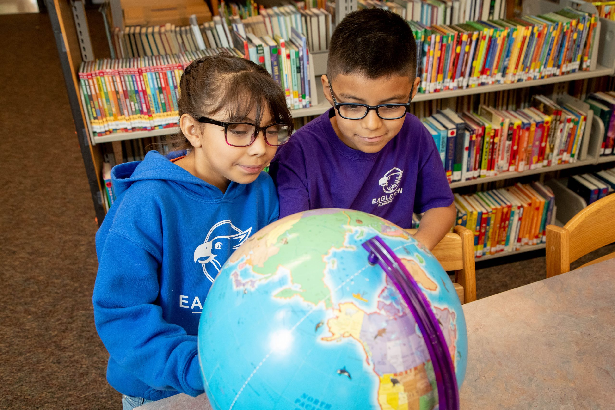 Two kids wearing glasses while taking a look at a globe.
