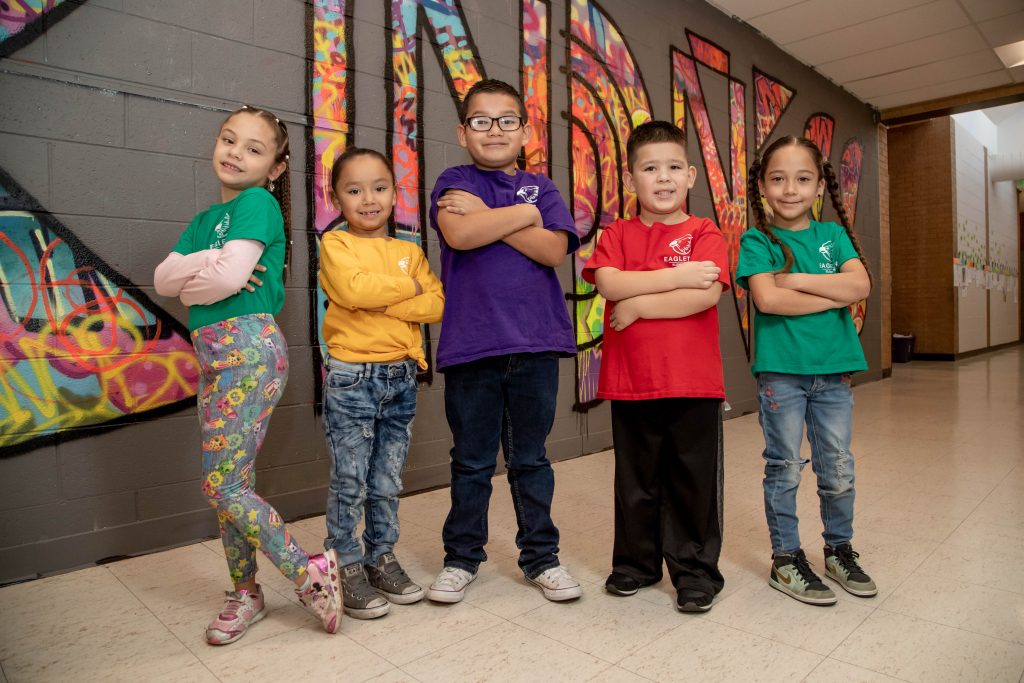 Group of kids crossing their arms posing for photo, colorful mural at the back