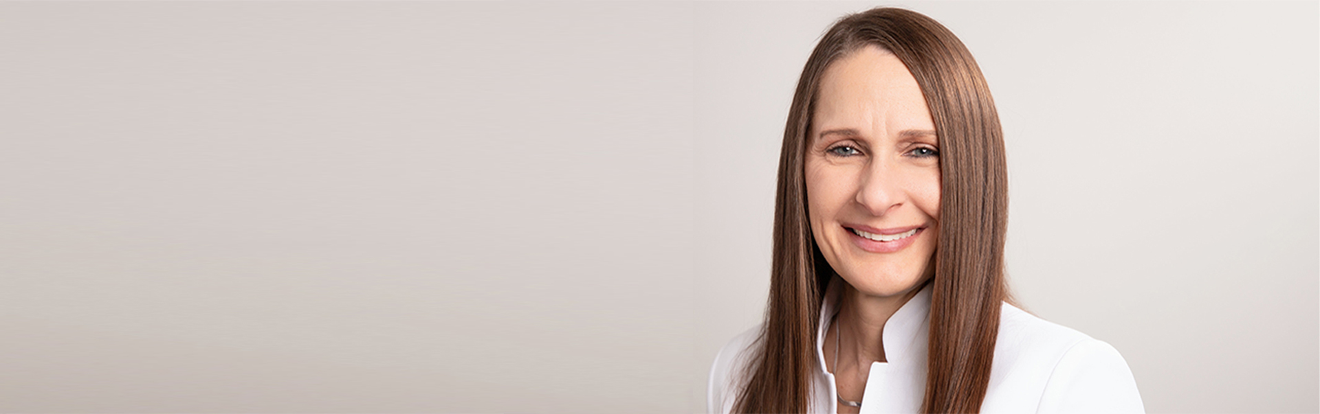 Dr. Sharp smiles while standing against light beige wall.