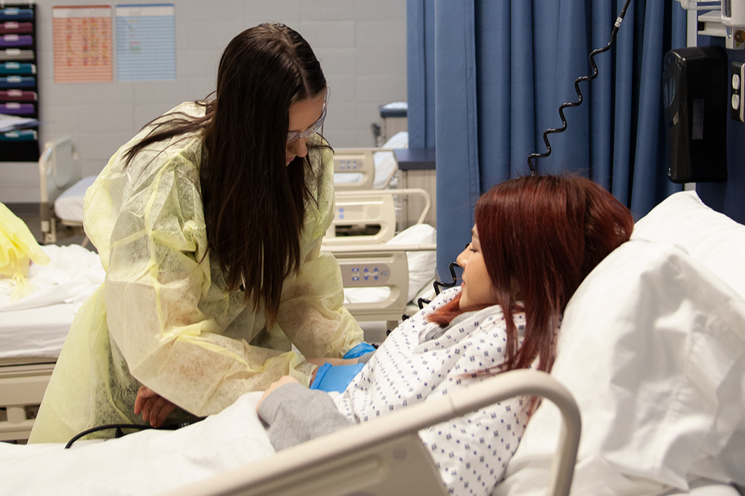 2 high school medical program students practicing patient care in a hospital bed