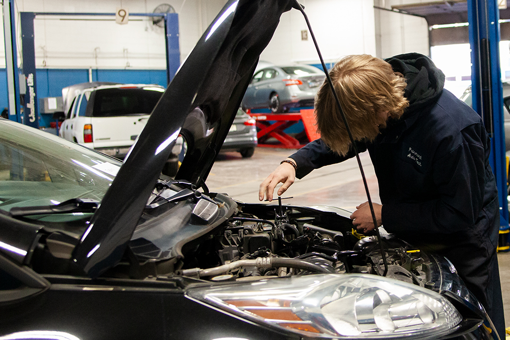 An automotves student working on the engine of a car with the hood up