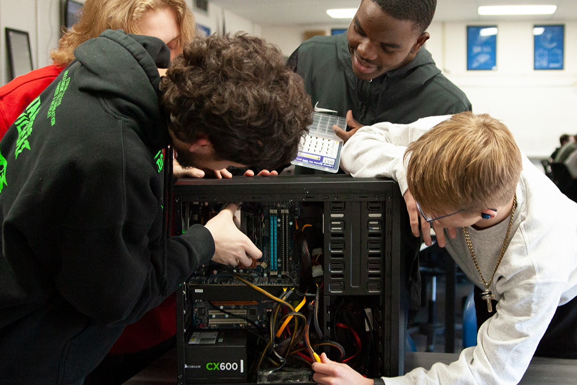A group of information technology students looking at the wiring inside a computer