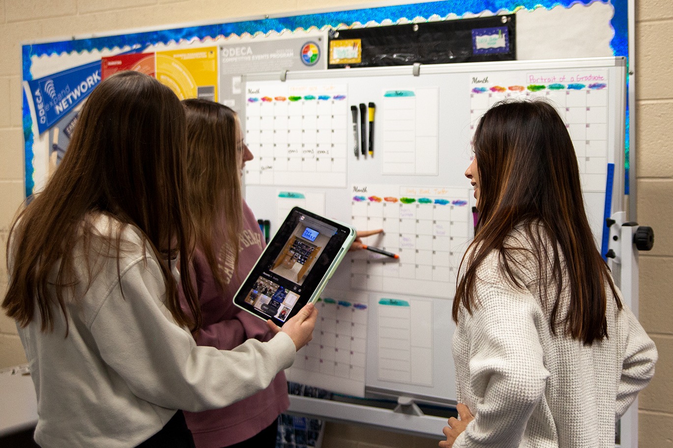 3 marketing students planning out events on a dry erase calendar