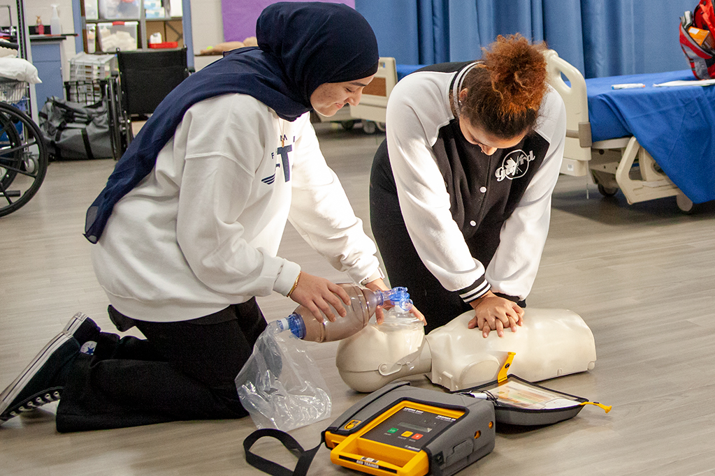 2 healthcare students adminstering CPR to a manikin