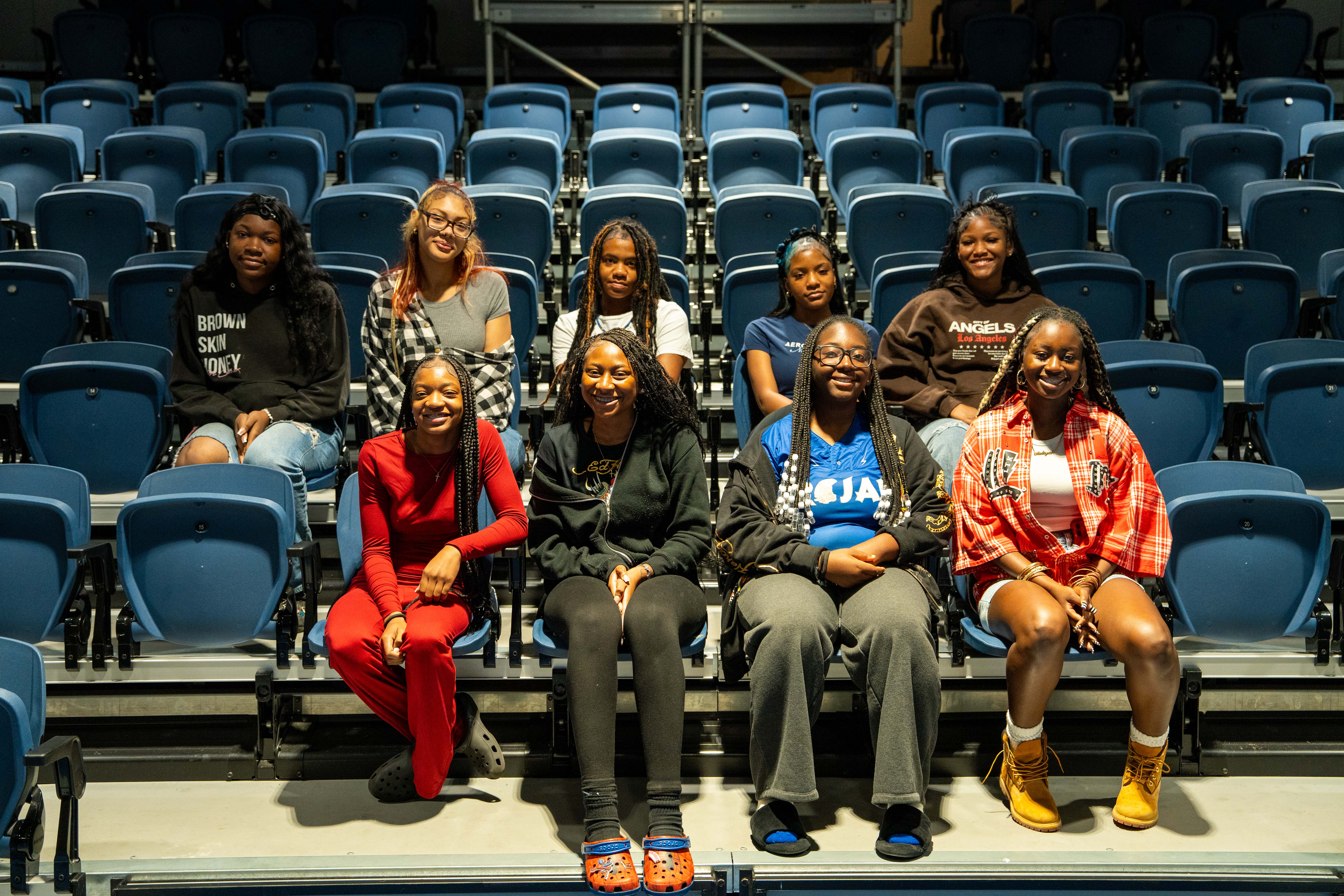 A group of people are seated in a theater, with some standing, on a stage with blue seats.