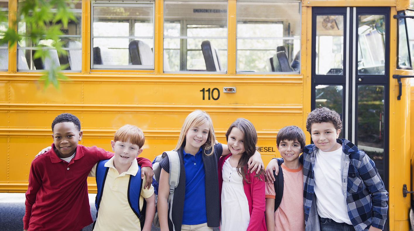 students posing in front of a school bus
