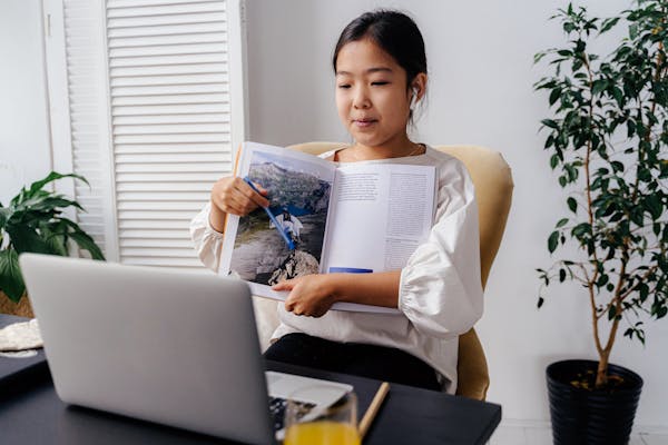 Young female student holds up a book to show her digital learning teacher via video call