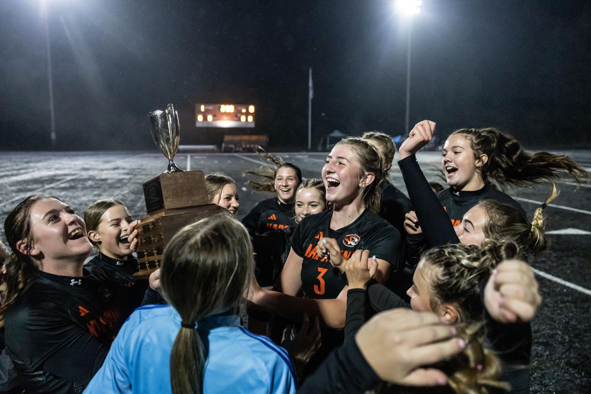 The High School soccer team celebrates on the field with the District Championship tropy