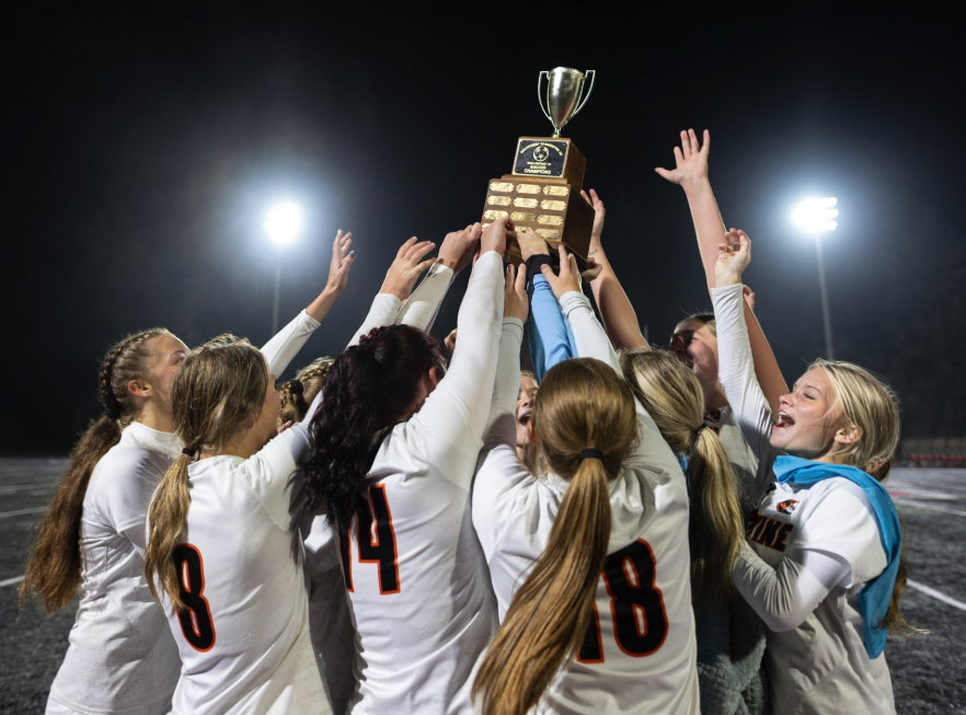 The girls soccer team hoists the district championship trophy after winning the match in shootout