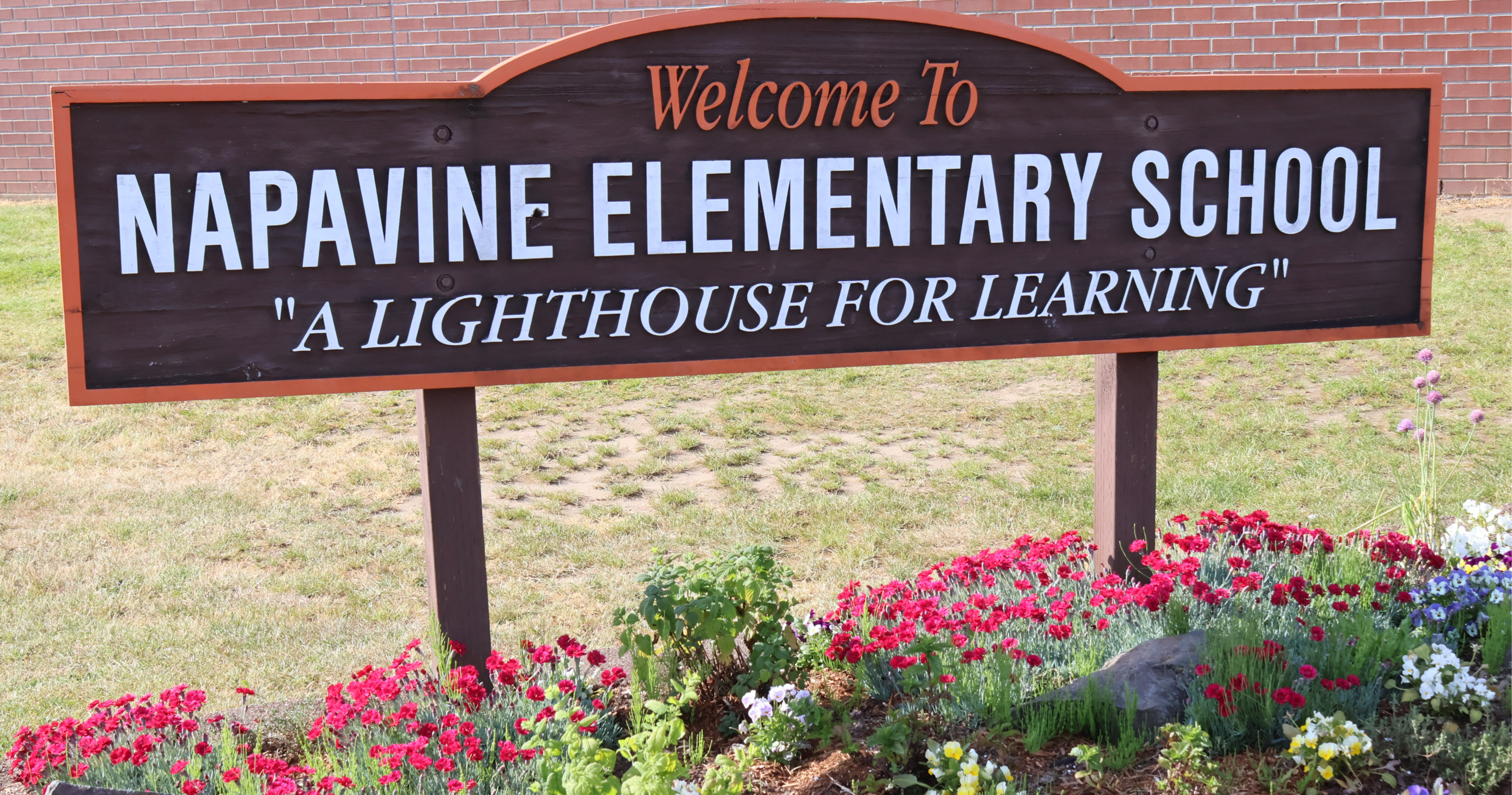 The Napavine Elementary sign stands in front of the Elementary/Middle School Gymnasium with flowers under neath