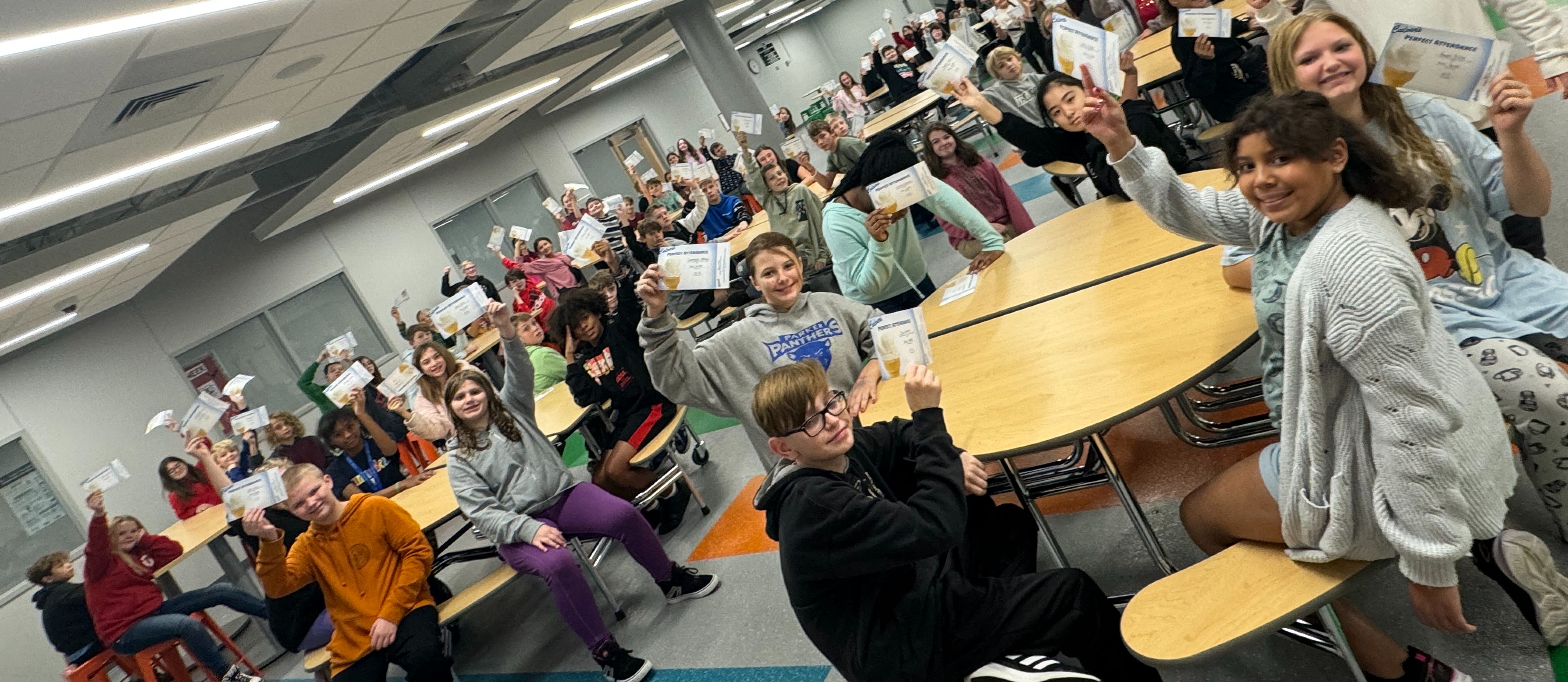 Students hold up their attendance awards in the cafeteria