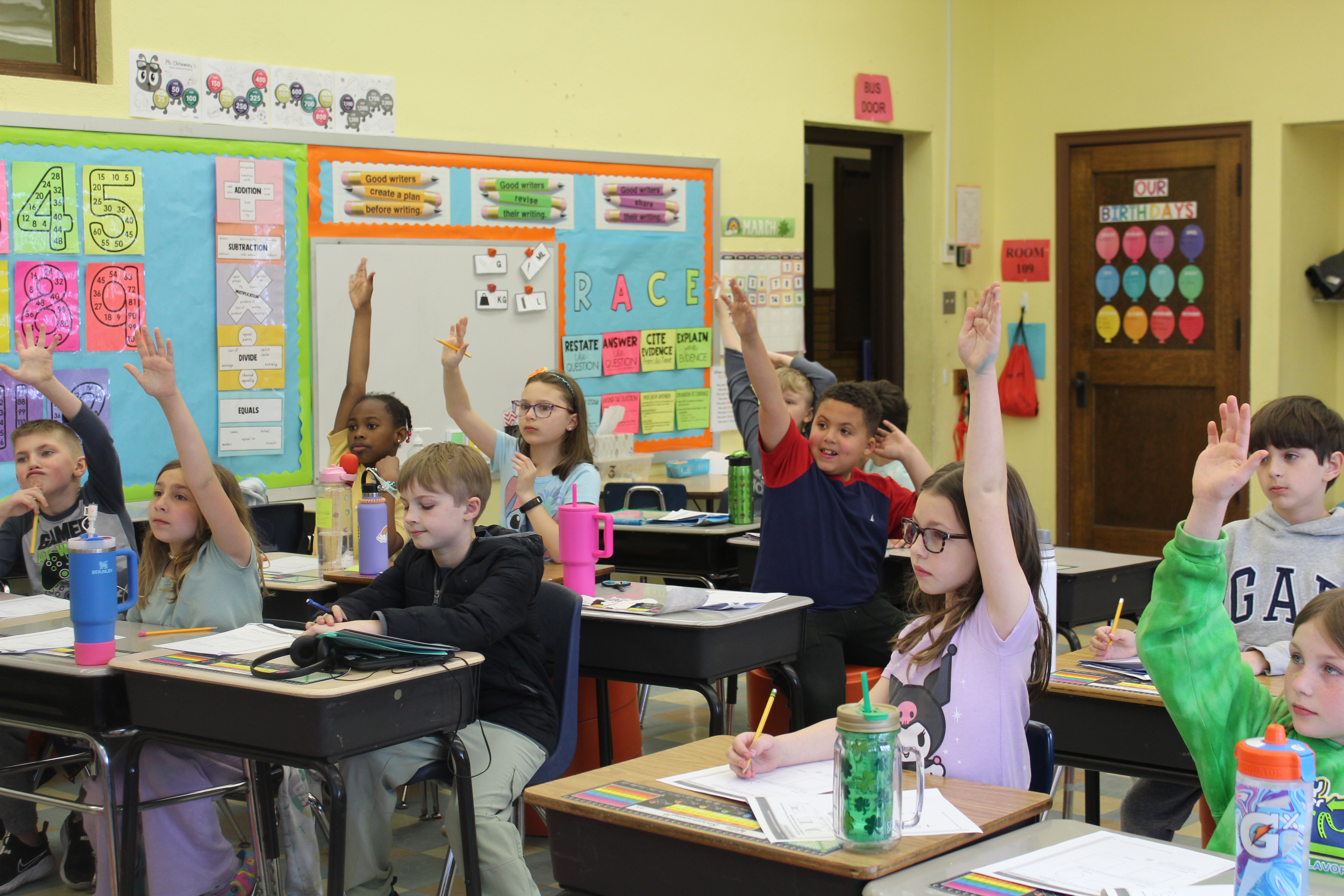 Students in classroom raising their hands.
