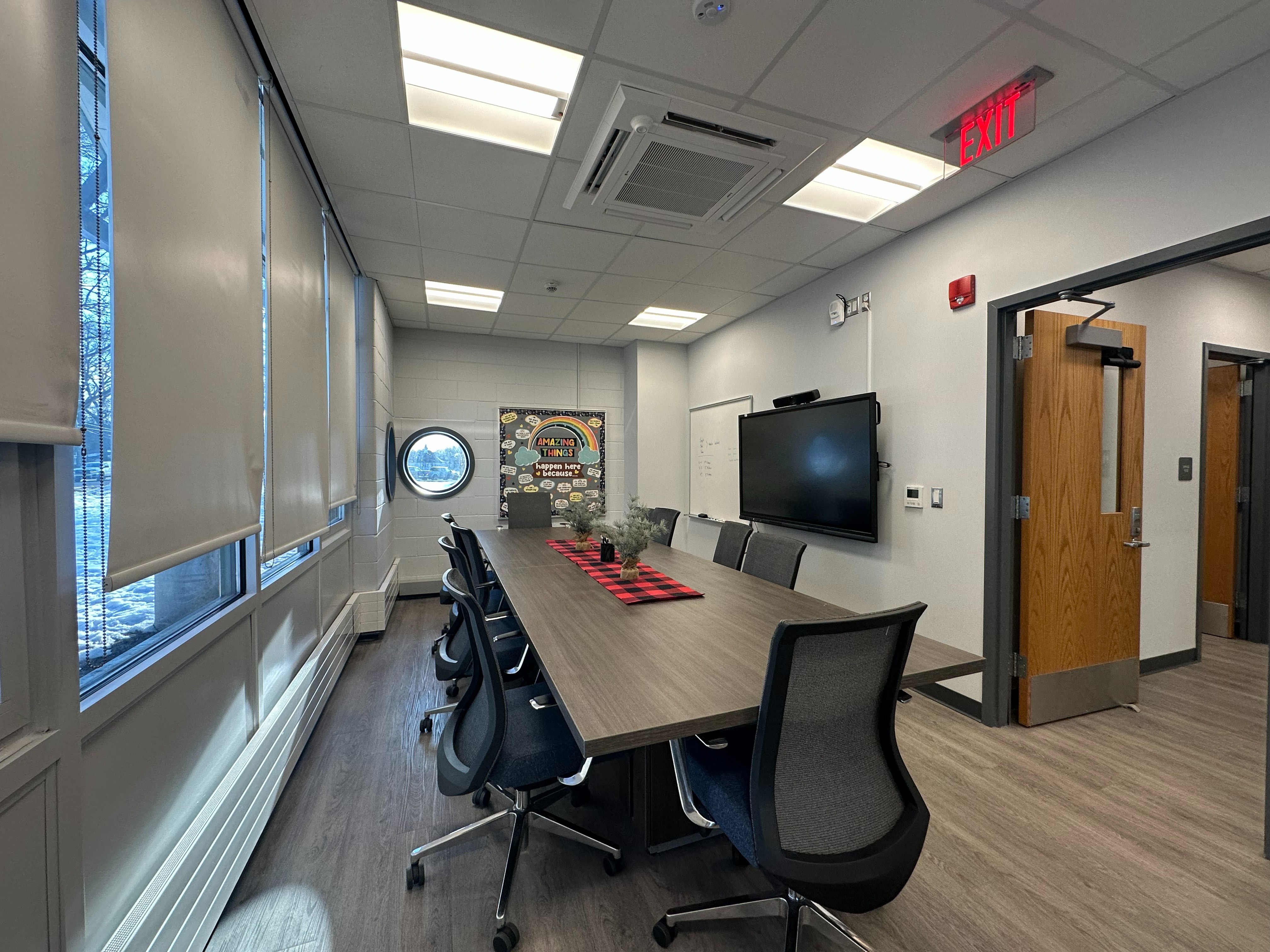 conference table and chairs with windows on left, and tv and doorway on right.