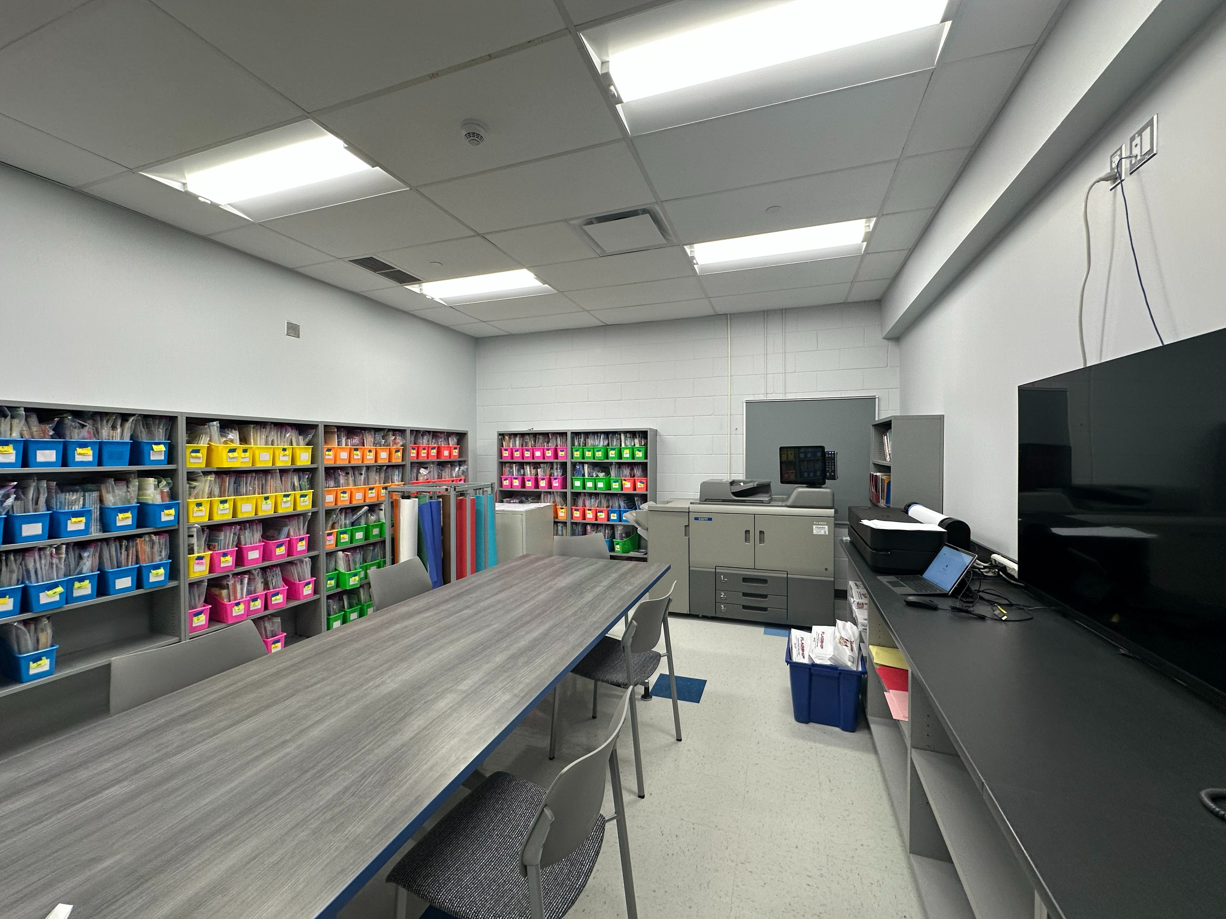 conference table with bookccases, a copier, a poster printer, lower cabinetry with open shelving, and a tv