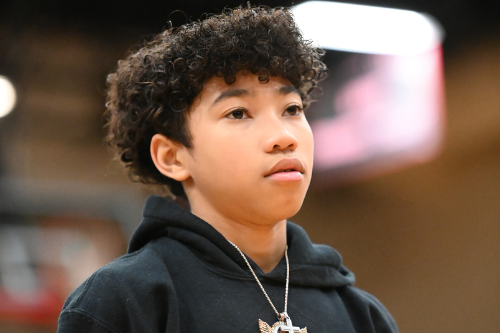A young person with curly hair wears a black hoodie with a white family design and a cross pendant.