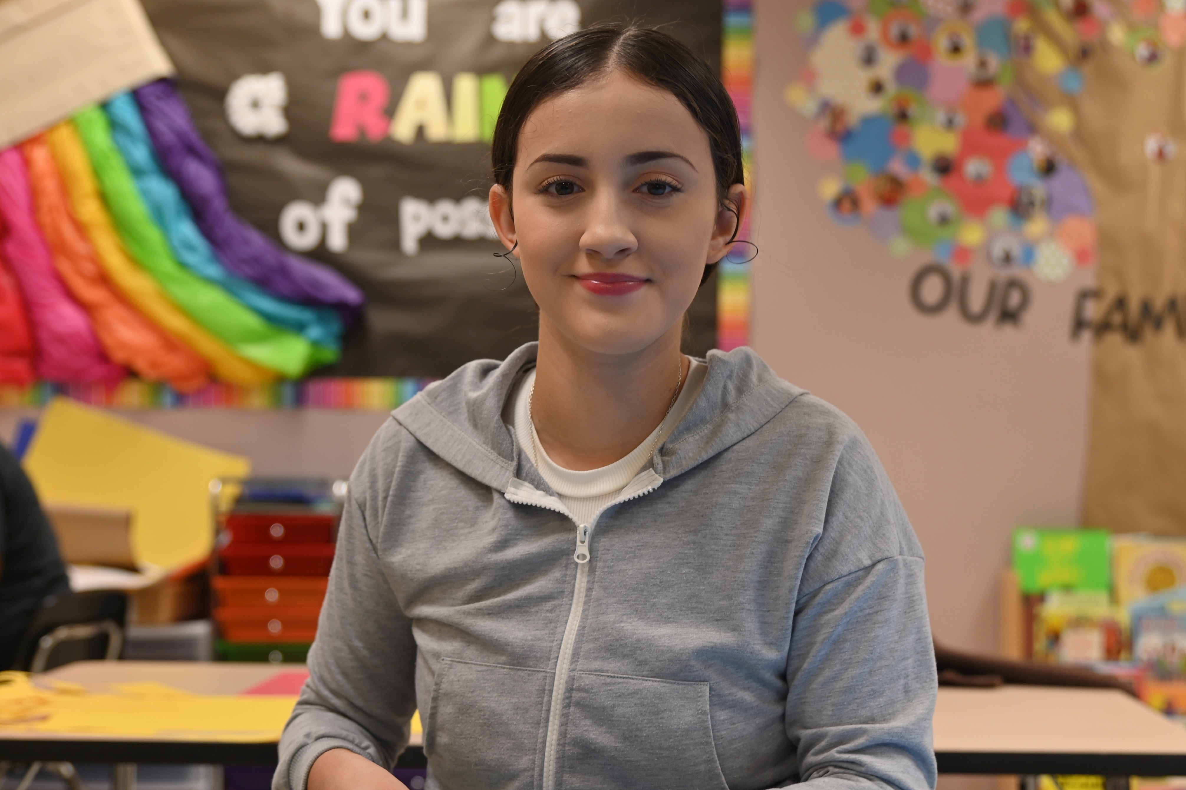 A young person uses scissors to cut out letters on a banner in a classroom.