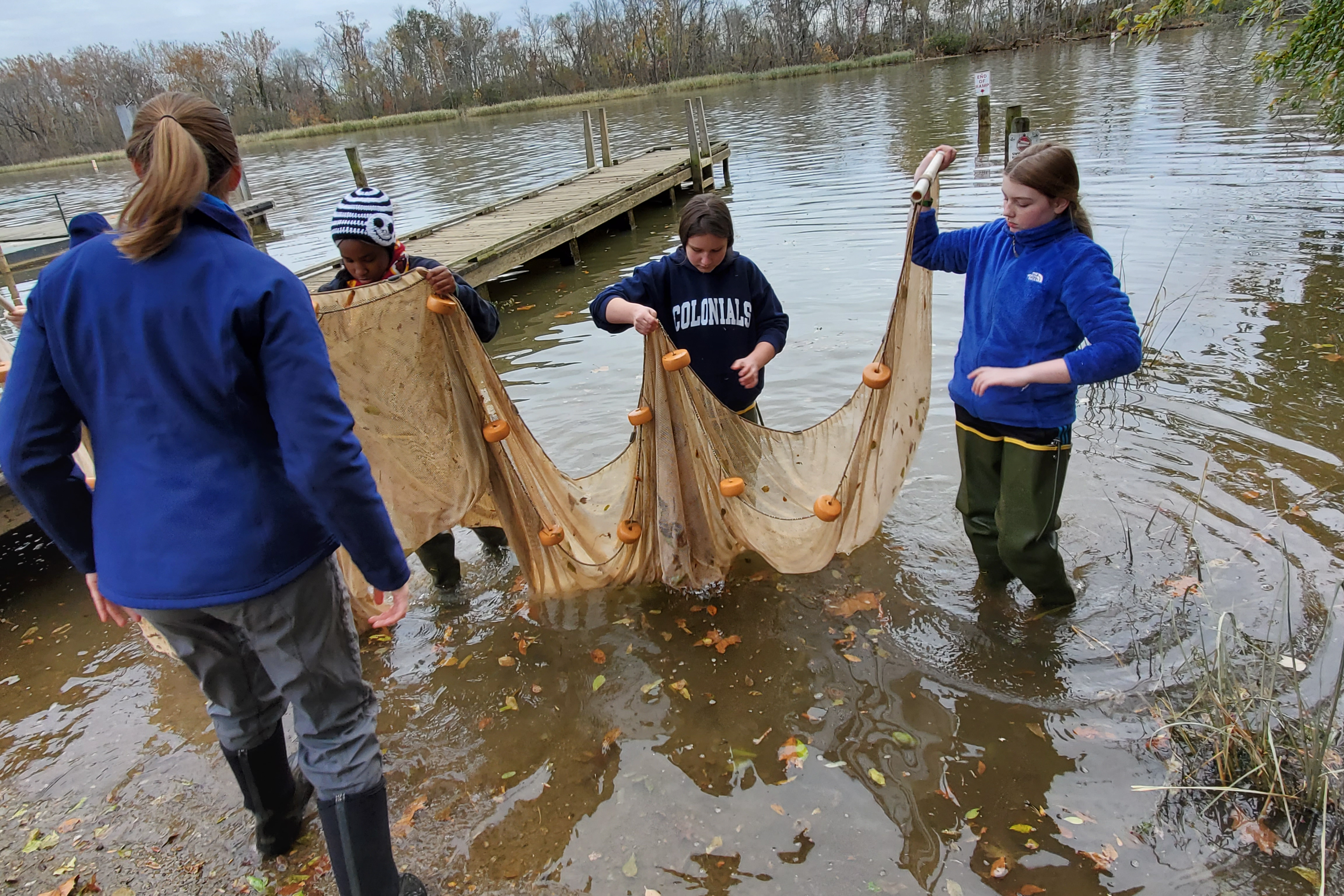 Students wearing waders stand in the water of the Appomattox River holding a fishing net together