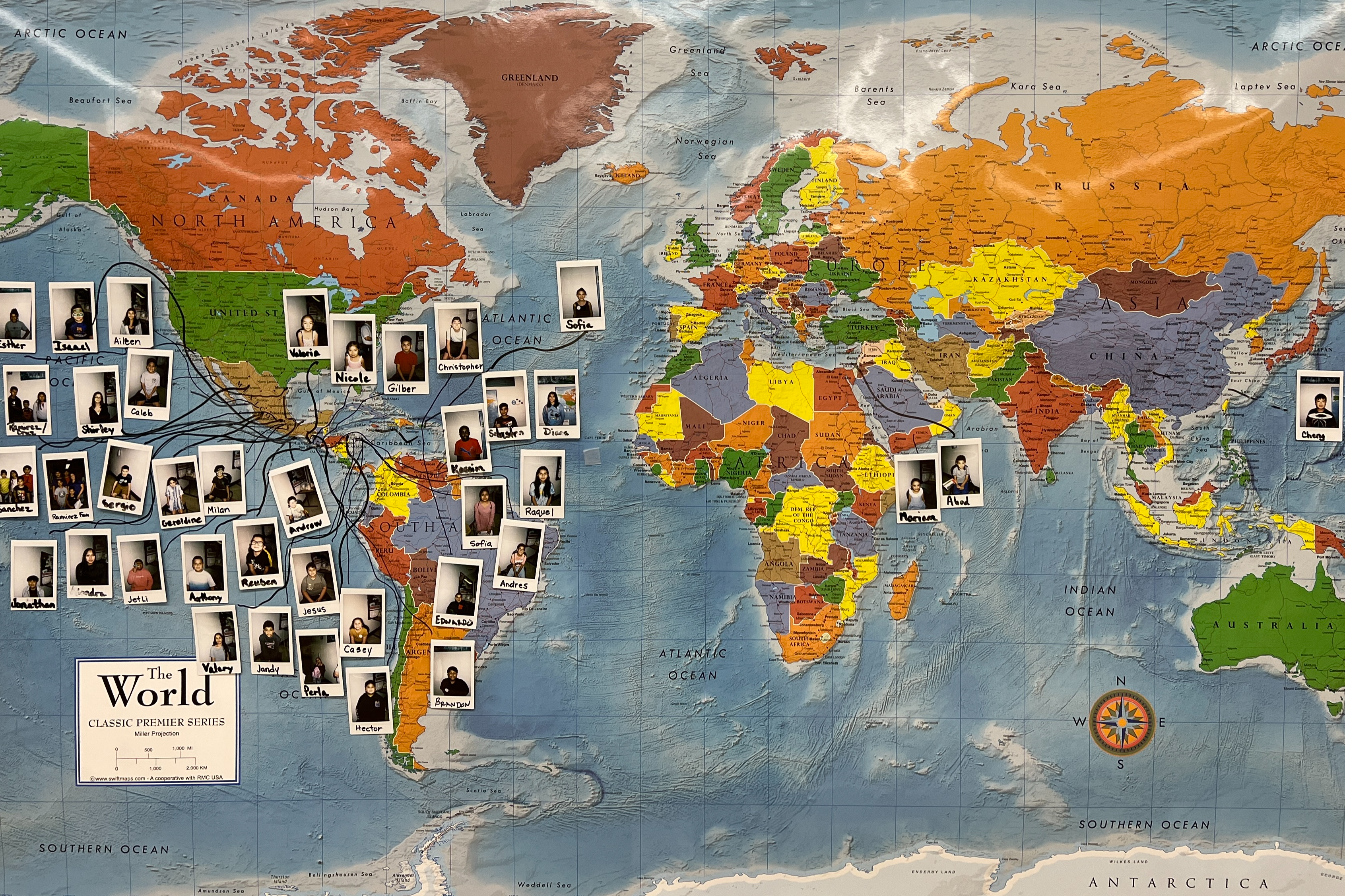 A map is hanging on a wall and ESL students' polaroid photos are pinned to the map over their home countries