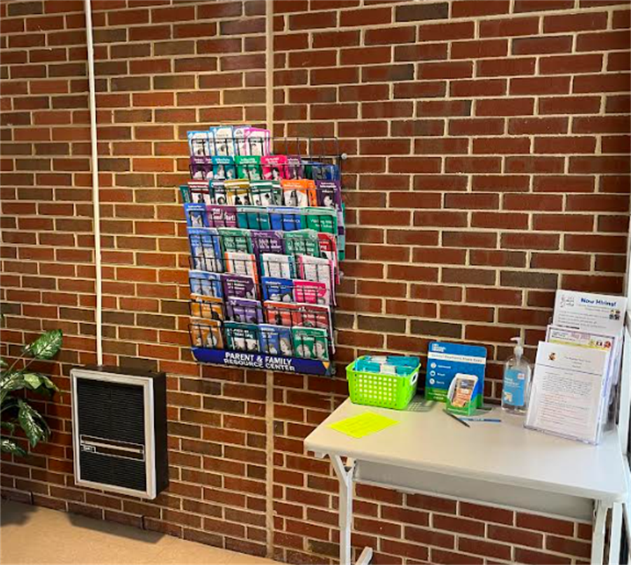 A wire rack full of multicolored pamphlets is attached to a brick wall inside a school entrance