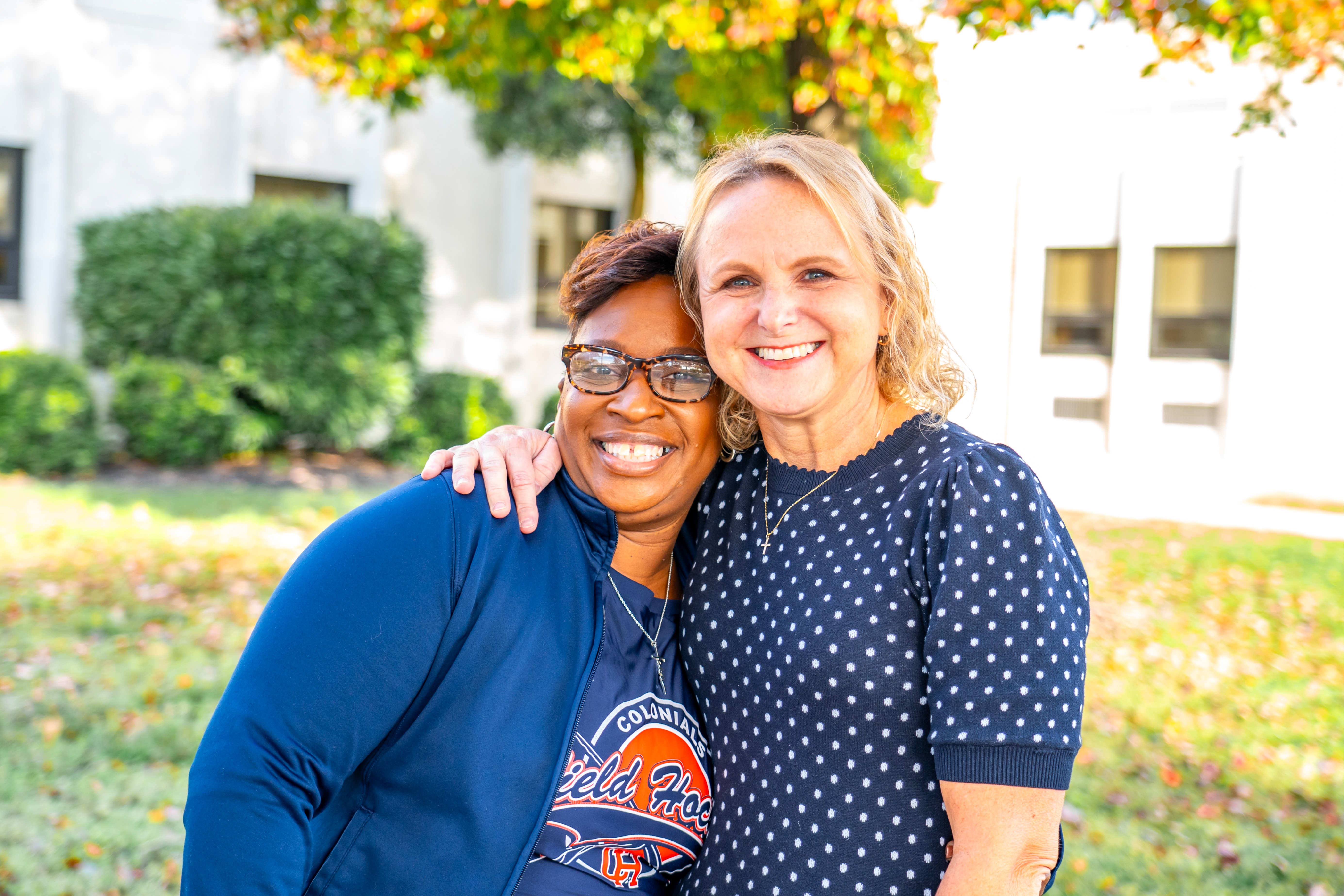 Middle aged black female teacher side hugging a middle aged white female teacher