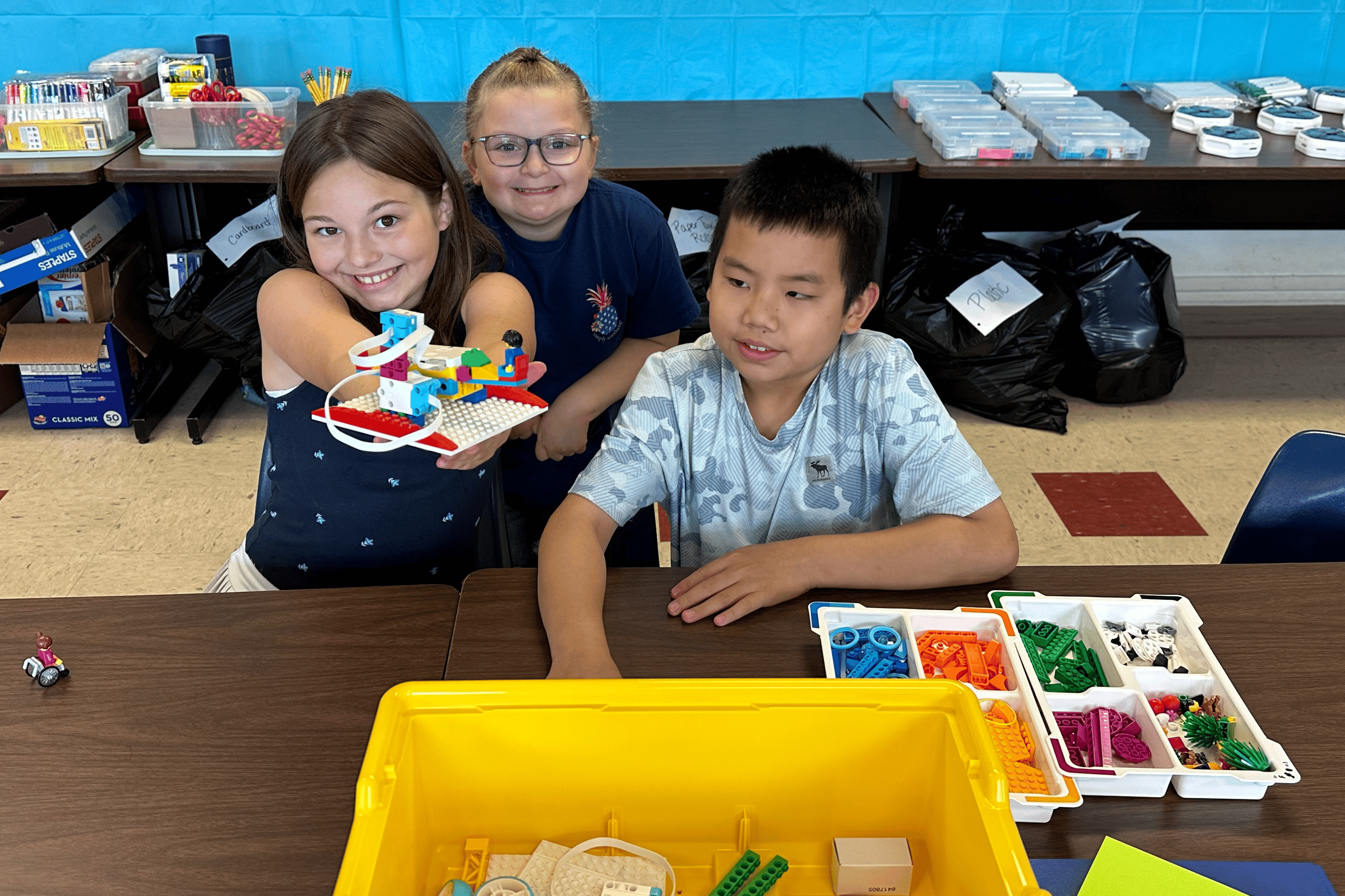 Three students show off the LEGO machine they built