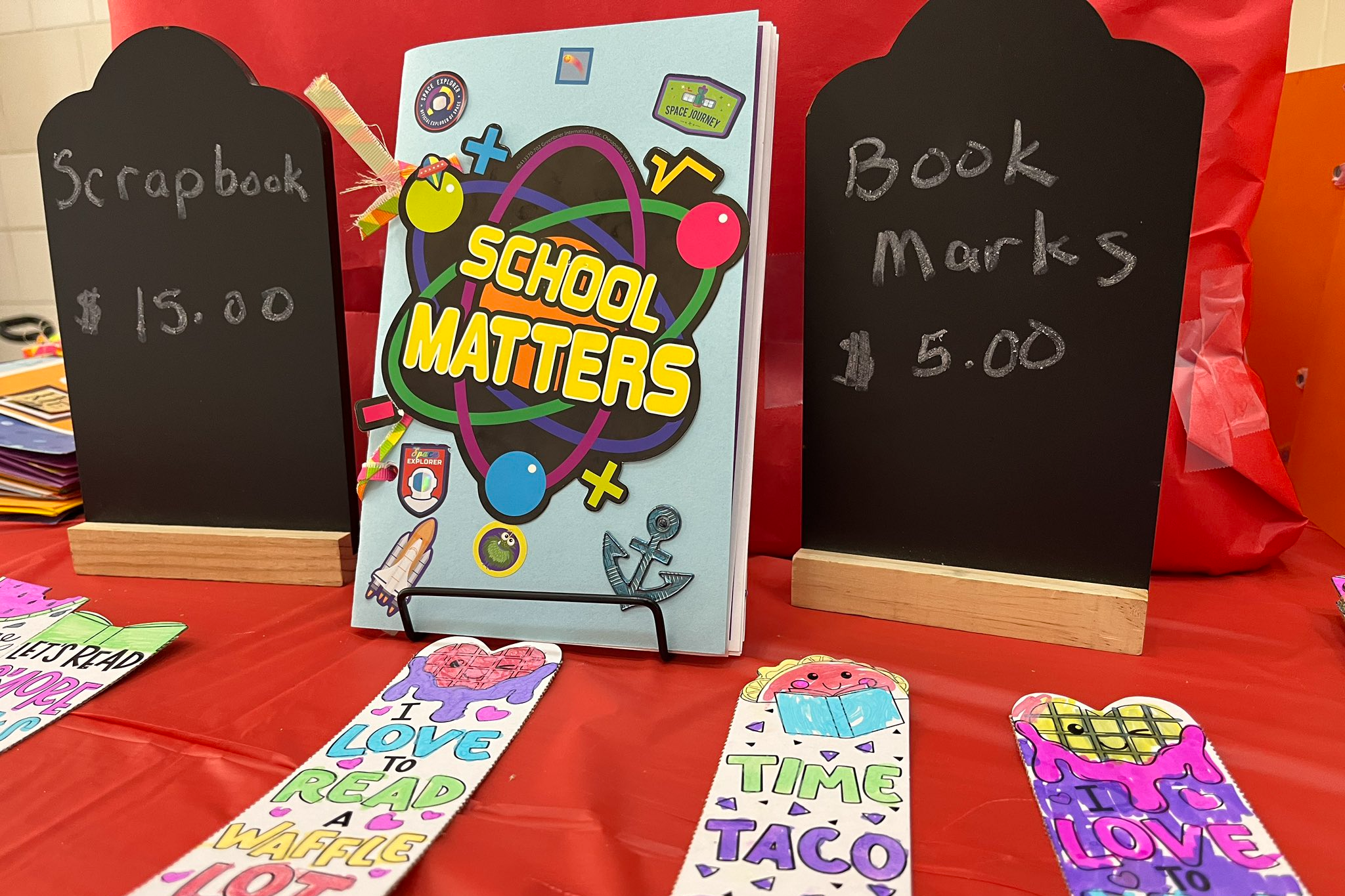 A table with bookmarks, a book, and two chalkboards. One chalkboard says "School Matters" and the other "Book Marks."