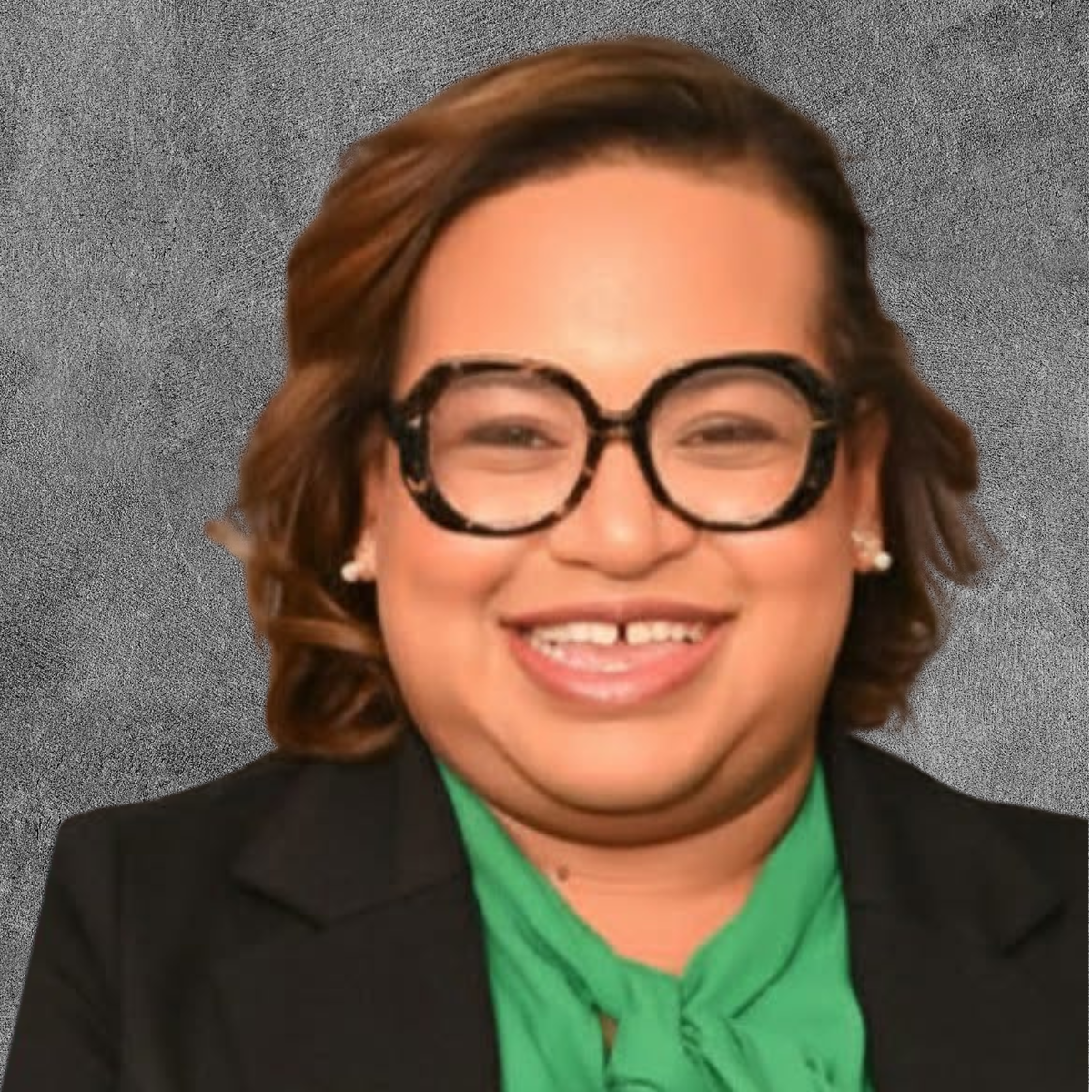 Woman in a green blouse and black blazer, smiling and wearing glasses, against a gray background.