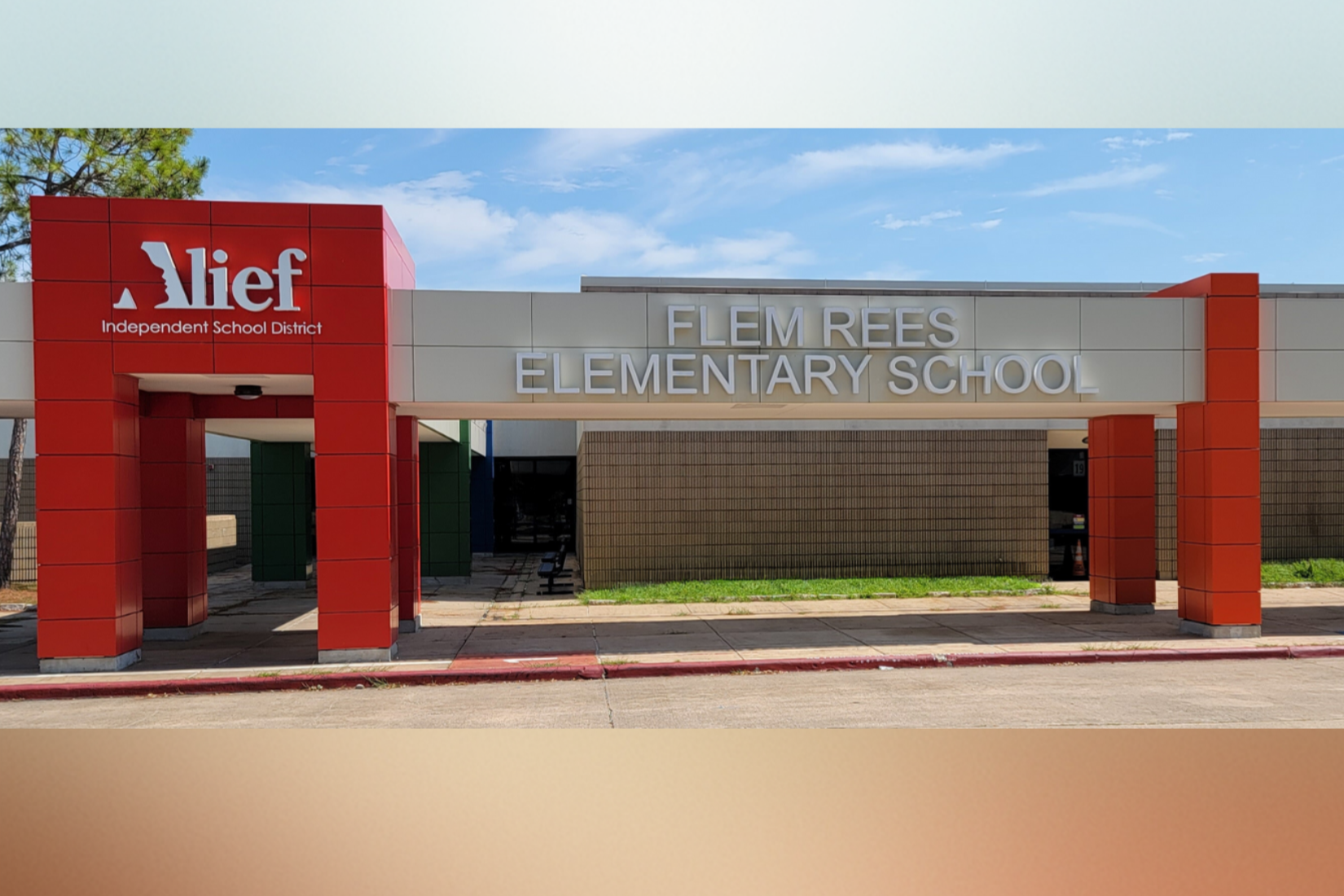 Entrance to Flem Rees Elementary School. A white sign with red columns and "Mie" on top. Background shows a blue sky and distant trees.