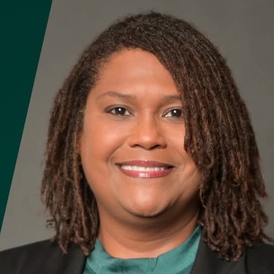 Woman with brown hair in dreadlocks, wearing black blazer and green shirt, smiling. Background is a gray and green gradient.