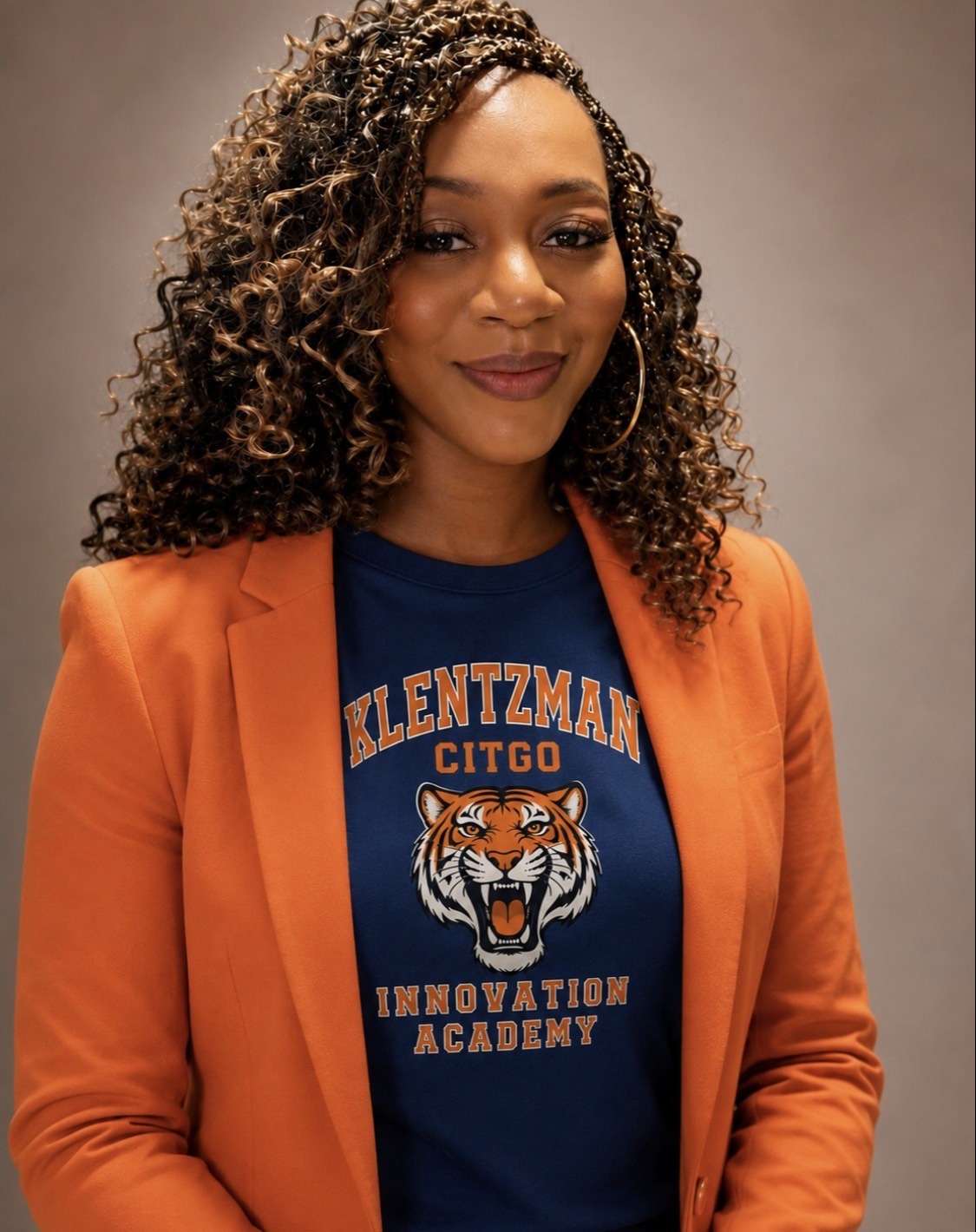 A woman with curly hair poses in an orange blazer, wearing a blue shirt with a tiger design.