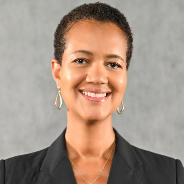 Person with short hair and short-sleeved black jacket smiles at camera. Light gray background.