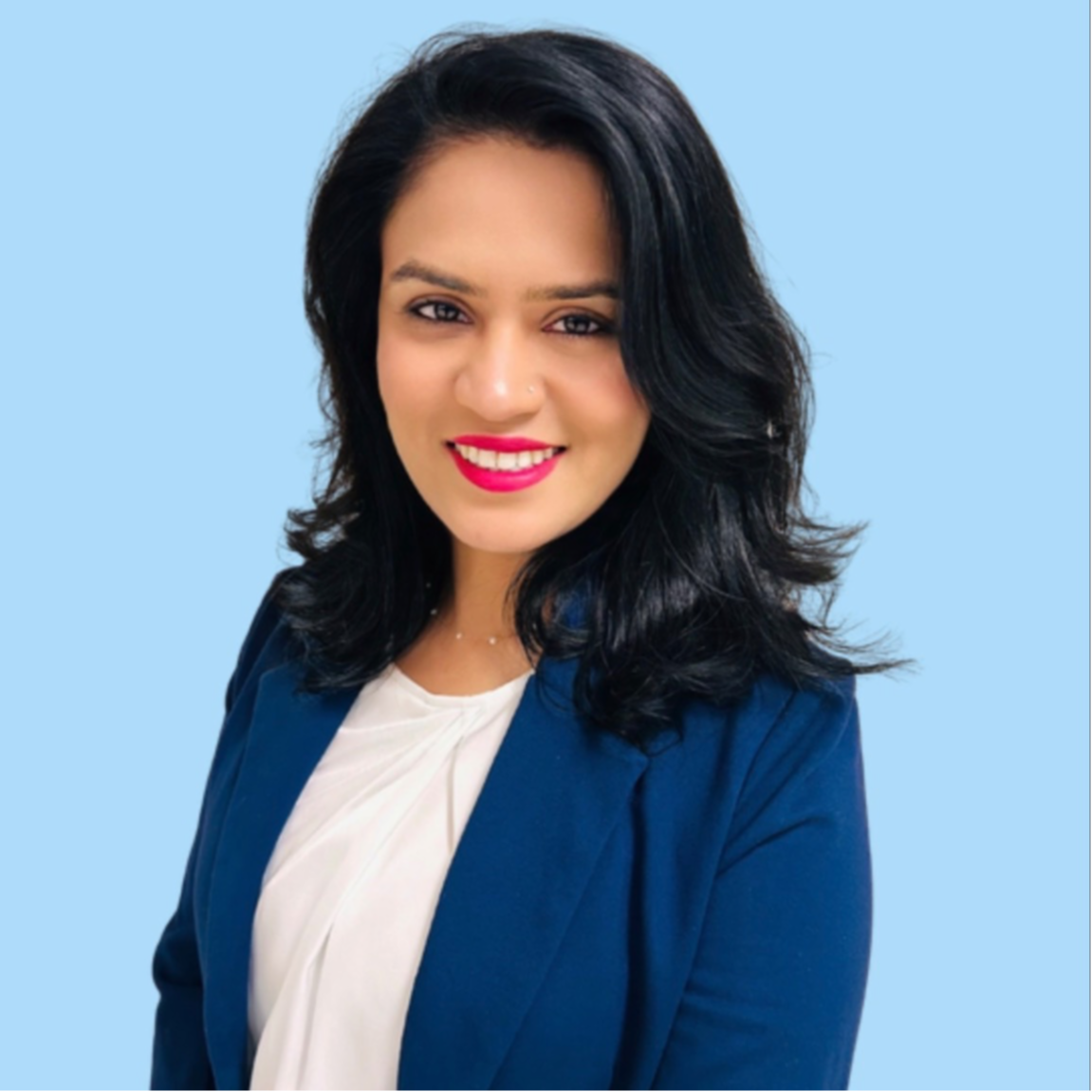 A woman with dark hair wearing a white blouse and a blue jacket poses against a light blue background.