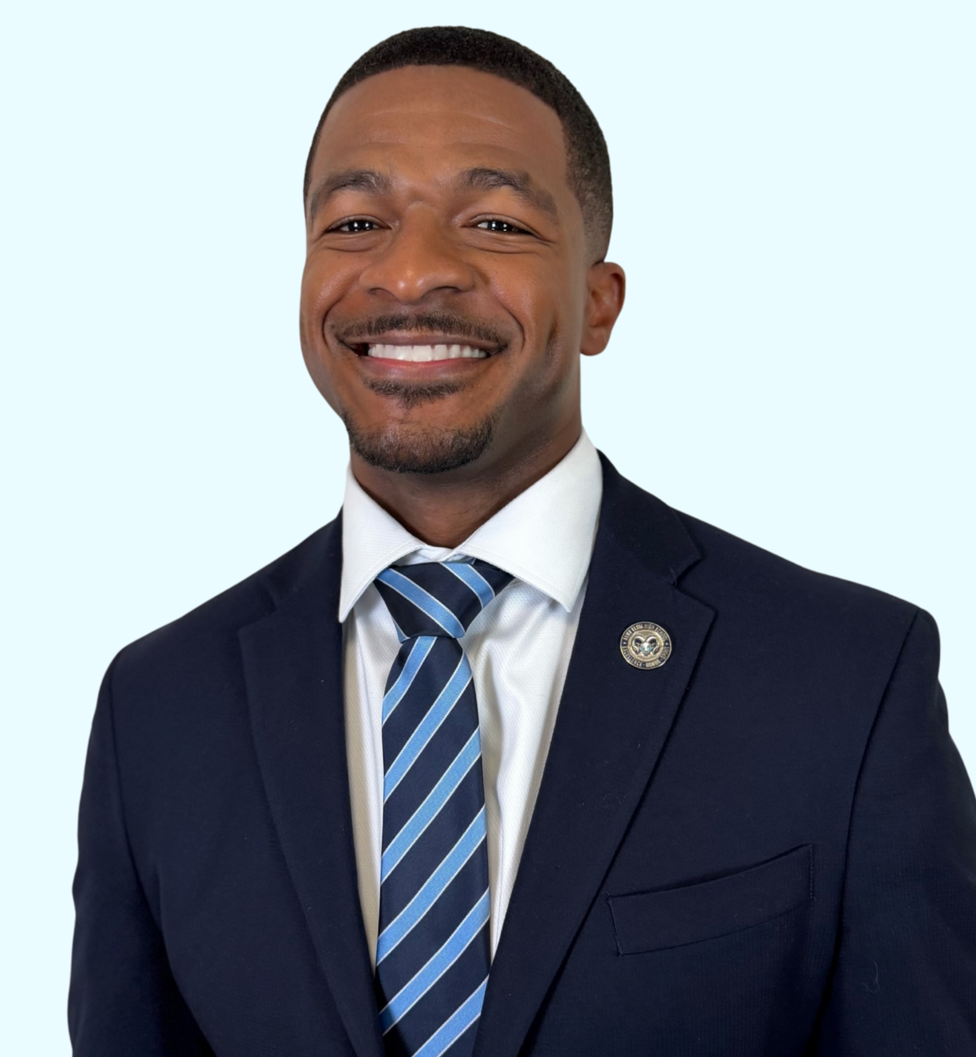 Man in a navy blue suit with a white shirt and blue striped tie, smiling and standing.
