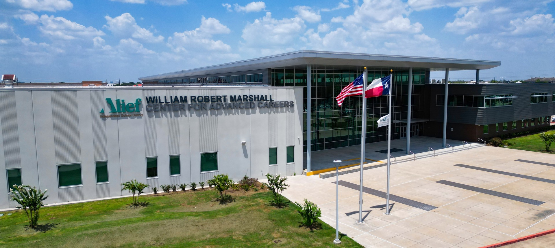 Large white building with flags on poles in front, text on side, and parking lot in front.