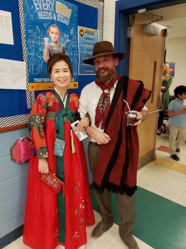 A man and woman dressed in traditional Asian clothing, posing for a photo at what appears to be an educational event.