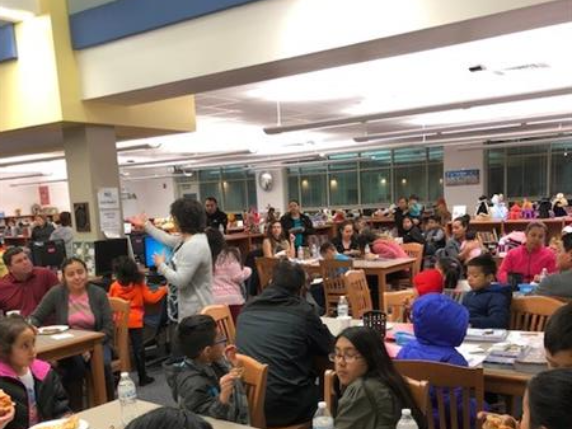 Children seated at tables, eating and conversing in a school cafeteria during lunchtime.