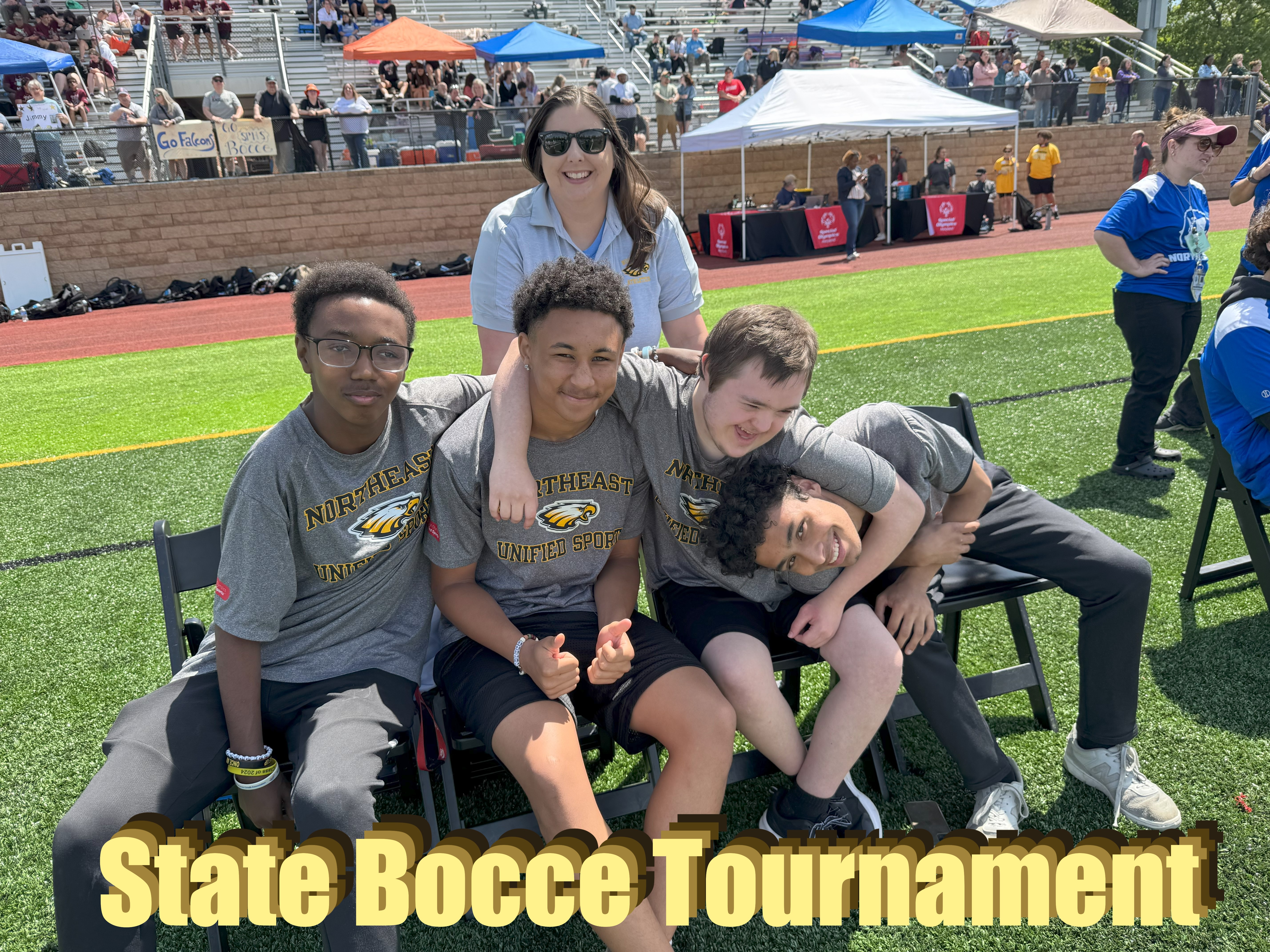 State Bocce Tournament  - 4 boys sitting in chairs with arms around thier backs smiling with a teacher standing behind them smiling