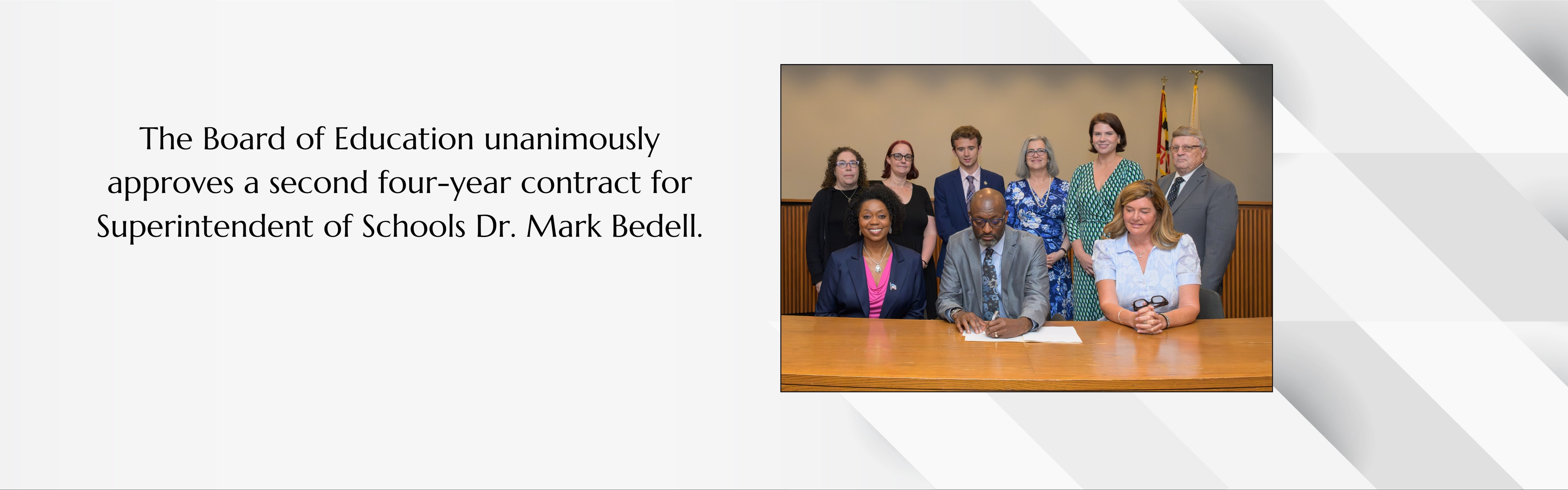 A group of people in suits and dresses sitting at a table, with a caption reading "Board of Education unanimously approves a second four-year contract for Superintendent of Schools Dr. Mark Bedell".