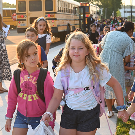 Elementary school students holding hands walking away from school bus