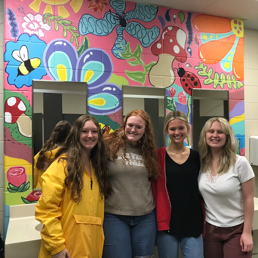 female upper school students and teacher on the restroom's sinks wall that was painted artistically